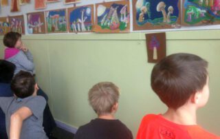 Children in art classroom lined up and looking at drawing of mushrooms