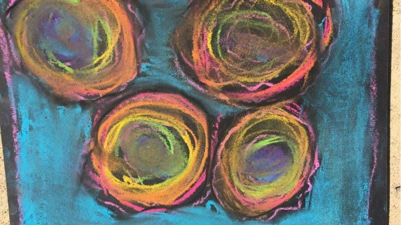 Colorful circles drawn with chalk on black paper floating in a turquois background