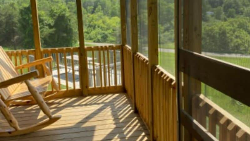 photo of screened in porch with a wooded rocking chair and view of green meadow and tree line