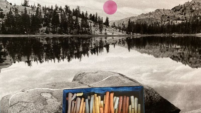 a box of color chalk pastels on a rock i the foreground. A river in the midgroud and trees and sky in the background.