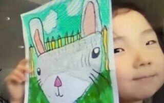 Smiling Young Girl of Asian decent holding a drawing of a rabbit