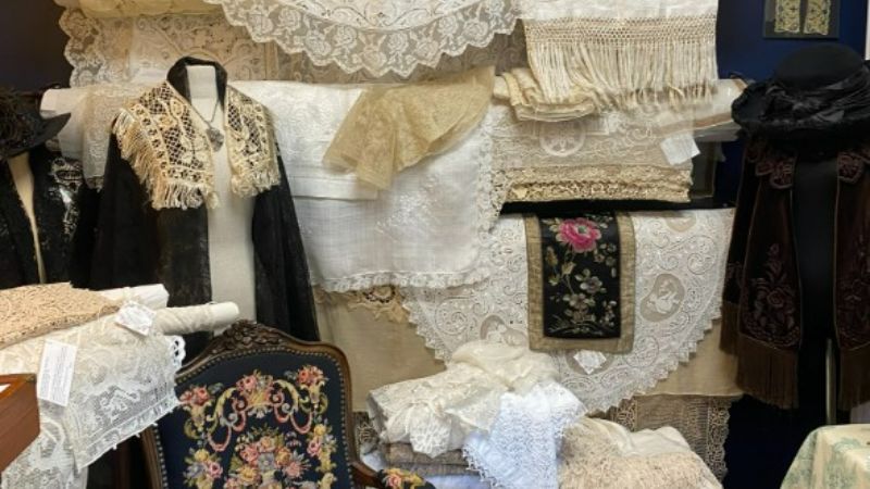 photo of many different kinds of antique lace hanging on a wall behind an antique rocking chair