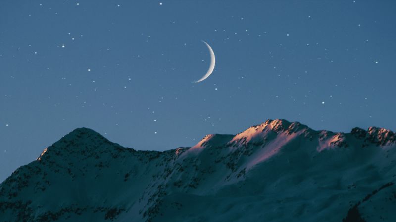 A stary night with a cresent moon over a mountain silhouette
