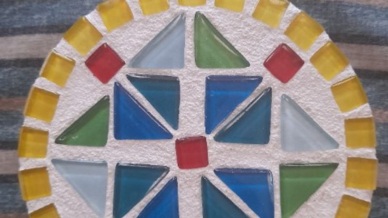 a round mosaic round tile consisting of light blue, dark blue triangles, red squares and yellow boarders.