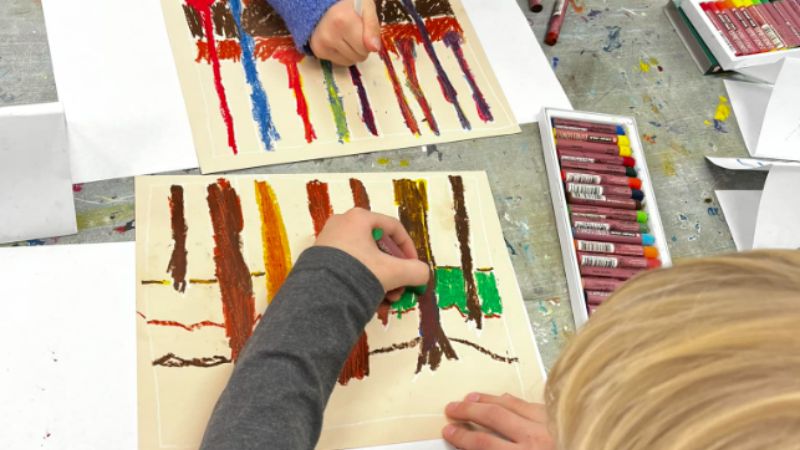 two children drawing colorful tree trunks with oil pastels
