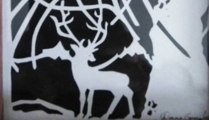 a black and white silhouette of a buck with a rack next to a thick tree trunk.