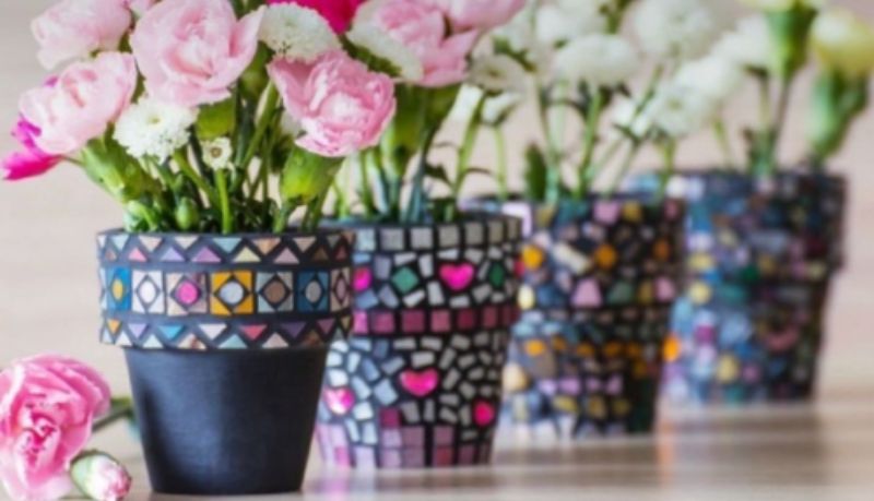four terracota mosaiced flowerpots in a row. the one closest to the viewer is in focus and they lose focus as they go back in space down the row. The pots have pink flowers.